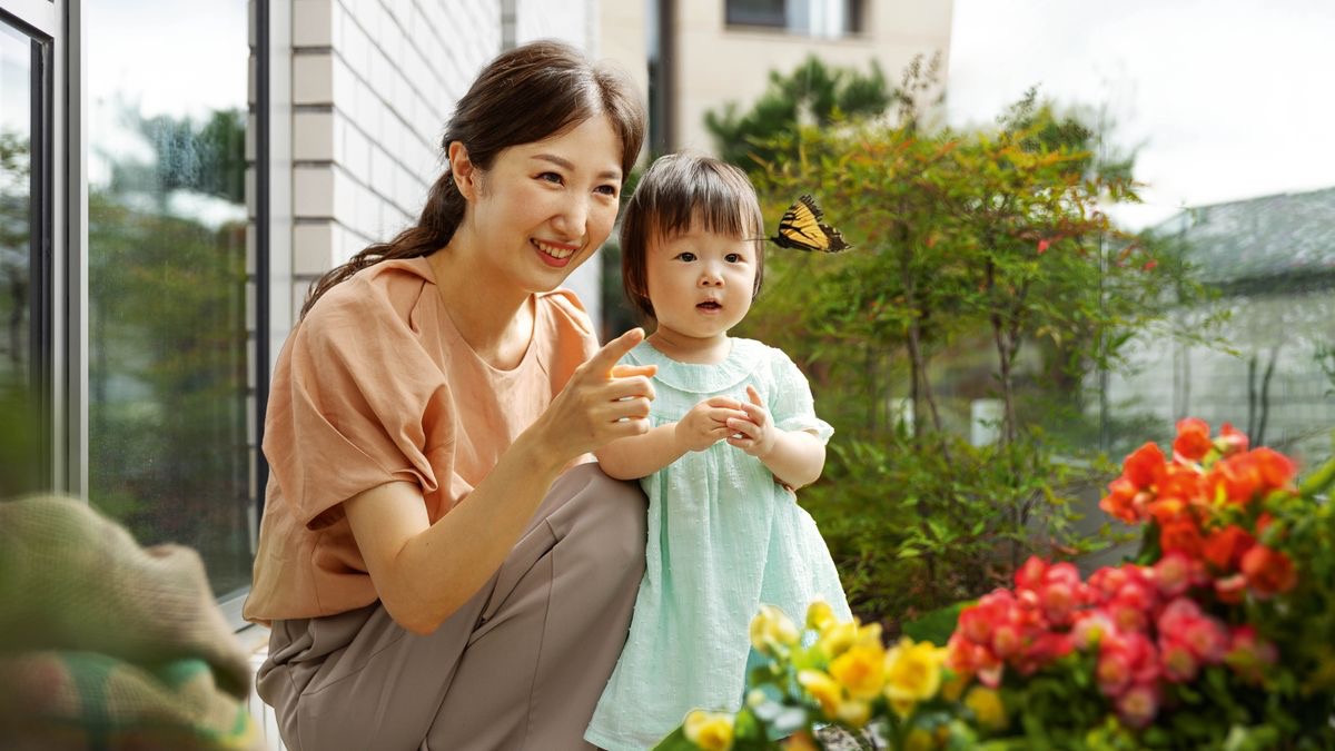 ある母親が街中の建物の外でチョウチョを指さし，小さな娘の注意を引いている。