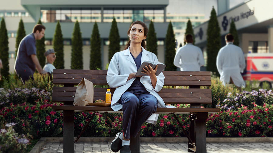 看護師の女性が昼休みに外で聖書を読み，空を見上げている。