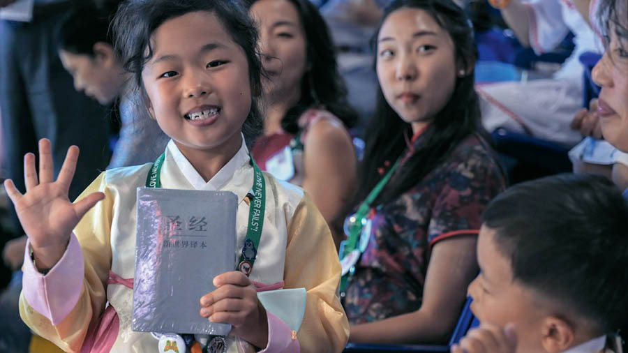 Picture from the video ‘‘Love Never Fails’! International Conventions.’ The little girl happily holding the New World Translation Bible in her hand’ that they just give her.