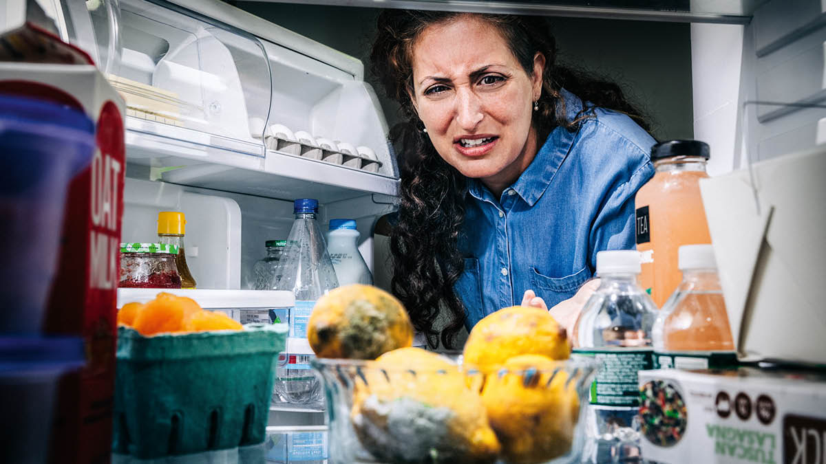 Una mujer mira con asco unos alimentos podridos que hay en la nevera.