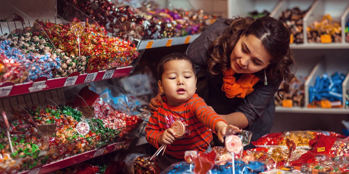 Een moeder in een winkel die nee zegt tegen haar zoontje als hij een snoepje wil pakken