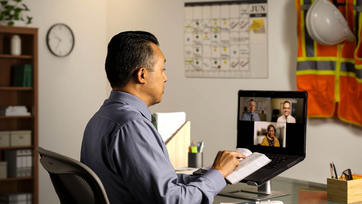 Twee ouderlingen brengen ’s avonds laat via videoconferentie een herderlijk bezoek bij een zuster. Een van de ouderlingen leest uit de Bijbel voor. Voor hem aan de muur hangt een kalender vol afspraken, met daarnaast een bouwhelm en werkkleding.