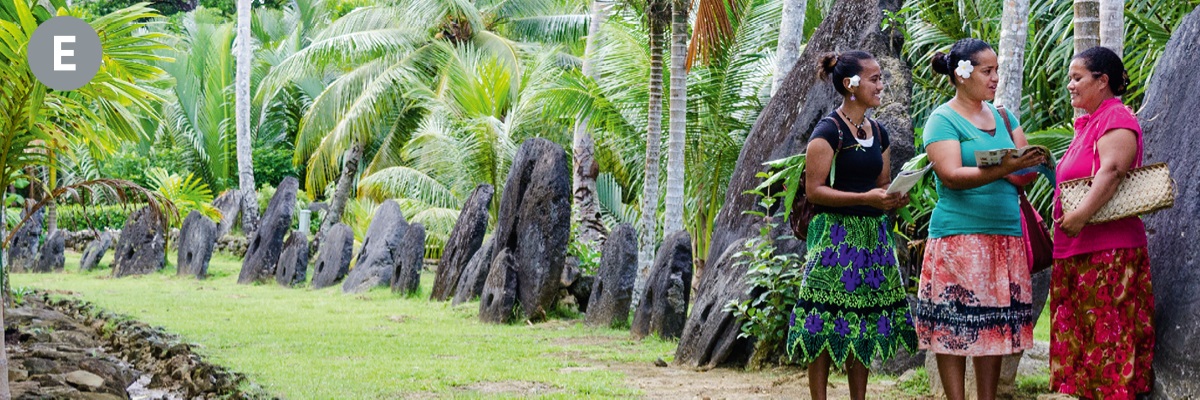 E. Dwie kobiety będące Świadkami Jehowy głoszą kobiecie stojącej przy ogromnym kamiennym dysku na wyspie Yap.