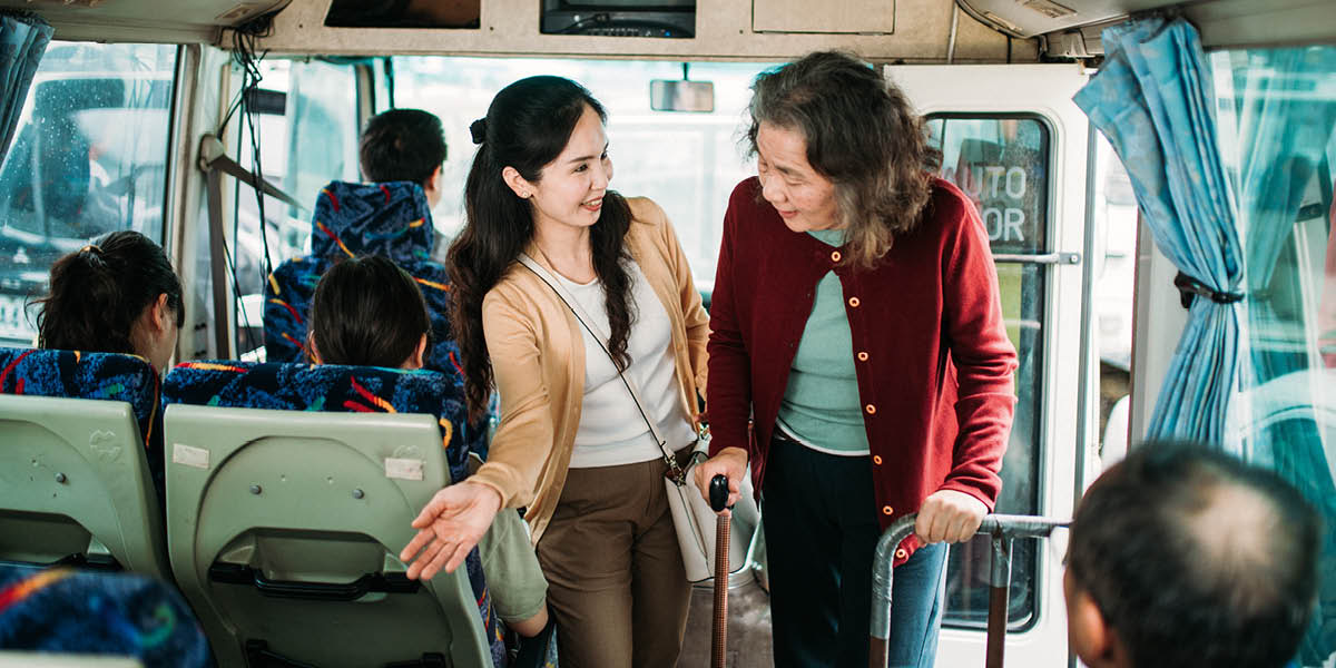 Kobieta proponuje starszej kobiecie swoje miejsce w autobusie.