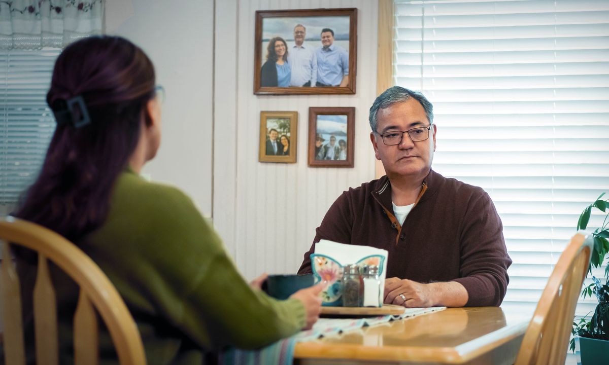 Banyalani ba lutse tafoleng ea ho jela. ’Mè o shebile linepe leboteng moo ba nang le mora oa bona ha ntate eena a shebile setulo se sa luloang.