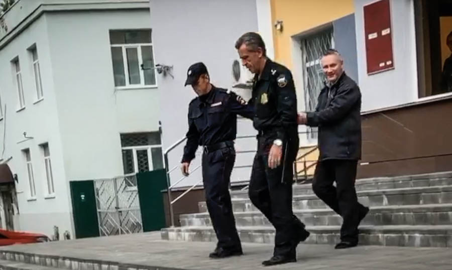 Litšoantšo tse hlahang videong ea ‘Puisano le Mora oa bo Rona Dmitriy Mikhaylov.’ Mora oa bo rona Dmitriy o tsamaisoa ke mapolesa a mabeli a mo fasitse ka lihanaboi.