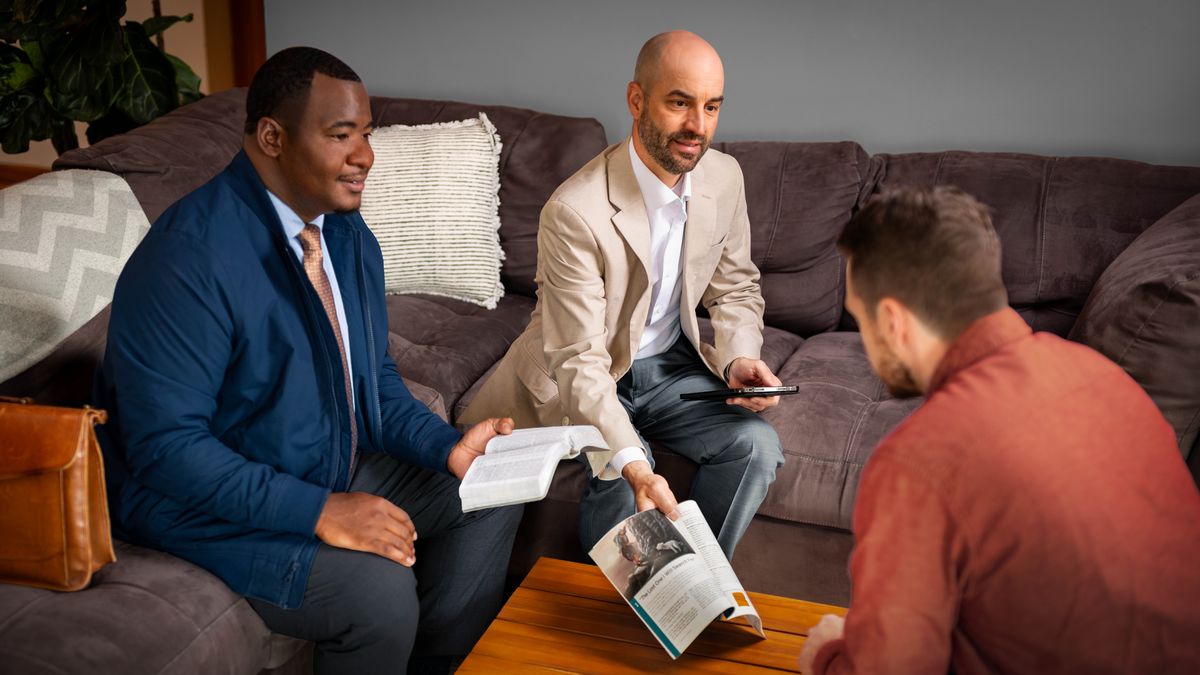 Baholo ba babeli ba etetse ntate ea neng a tlositsoe ka phuthehong. Moholo e mong o tšoere Bibele a e butse ha e mong a bontša ntate eo karolo e hlahang bukaneng ea “Khutlela ho Jehova.”