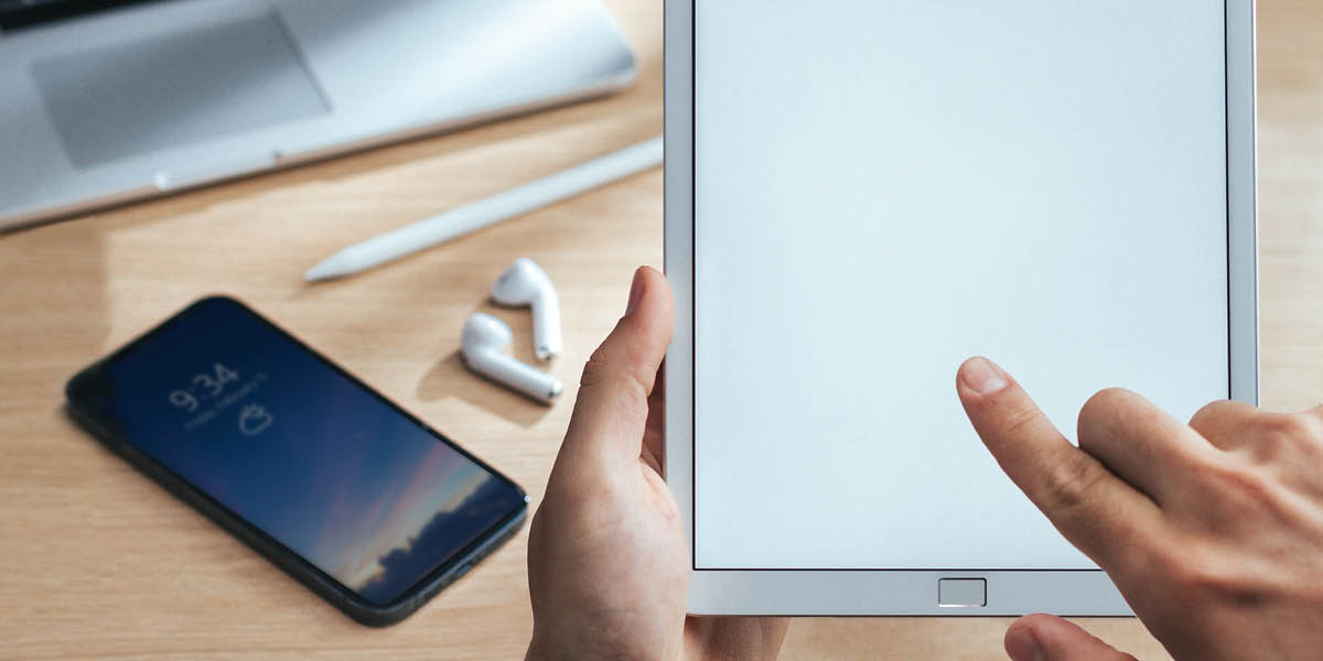 Saurang jalma keur maké tablét. Di méja aya gadget séjénna.