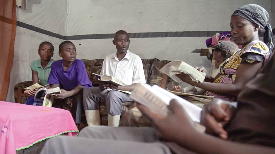 Gambar tina vidéo ’Ngawangun Imah nu Weweg—Jaga Budak Sadérék ti ’Hal-Hal anu Jahat.’’ Kulawarga di Afrika maca jeung ngabahas ayat-ayat jeung barudakna.