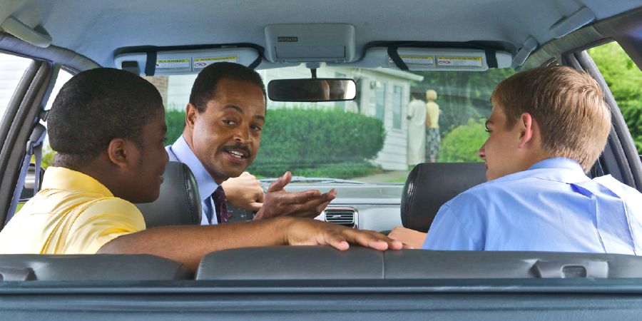 Dentro do carro, um irmão maduro conversando com dois jovens irmãos.