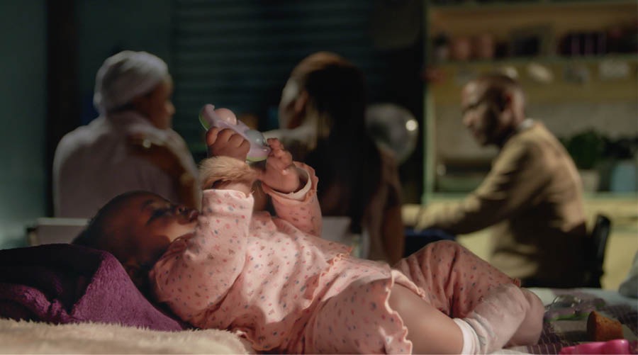 Una bambina nel leto doperando un amuleto nel pulso. In fondo, so mama la ze drio parlar col casal che el stùdia la Bìblia con ela.