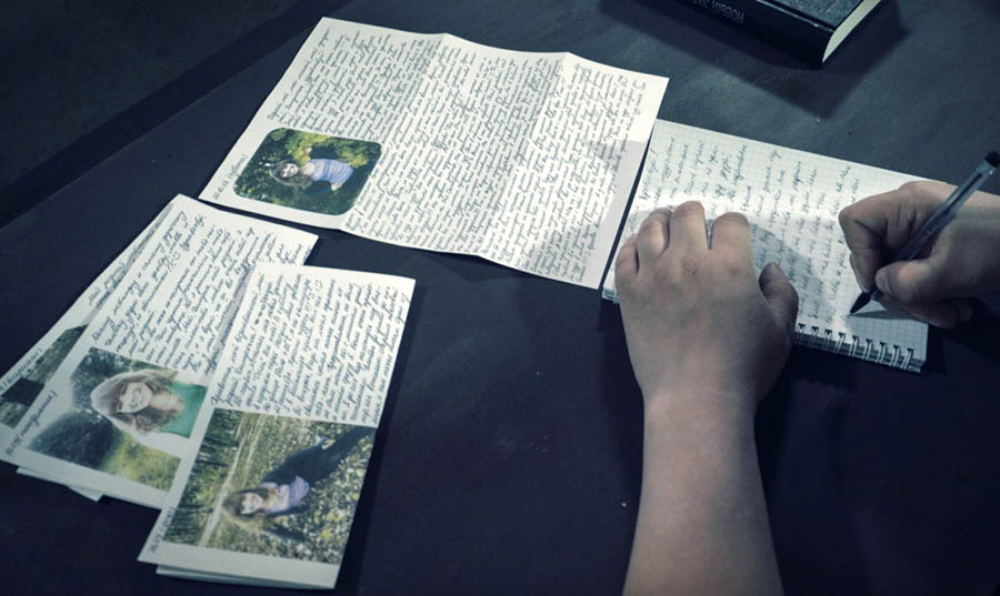 Una parte del vìdeo ‘Intervista col fradel Dmitriy Mikhaylov.’ Dmitriy l’è drio scriver una carta intanto che l’è in preson. Ghen’è diverse carte dela so dona sora la tola.