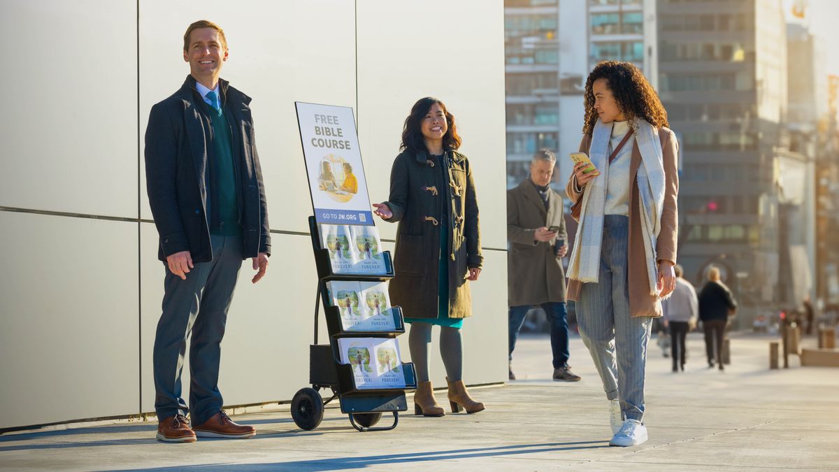 Un casal l’è col careto che el ga la stampa “Impara la Bìblia sensa pagar gnente”. Una dona la passa davanti a lori.