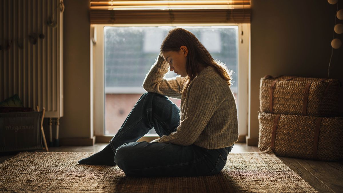 Una gióvena la ze triste, sentada par tera e cola testa bassa.