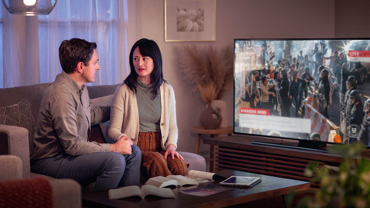 Un fradel e una sorela i ze drio vardar le notìssie nela TV sora protesti. Lori i ga una Bìblia e altre publicassion sora la tola.