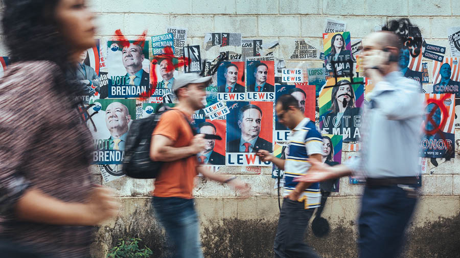 Persone le passa darente de un muro pien de foto de polìtichi.